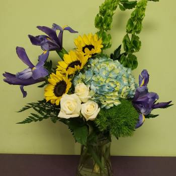 Bouquet of sunflowers, white roses, blue hydrangea, and purple irises in a glass vase