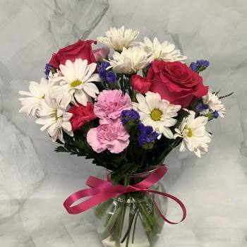 Bouquet of red roses, white daisies, and pink carnations in a glass vase