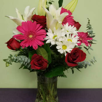 Bouquet of red roses, pink gerberas, white lilies, and daisies in a glass vase