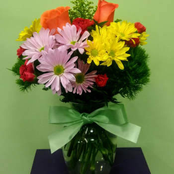 Bouquet of orange roses, daisies, and red carnations in a glass vase with a ribbon