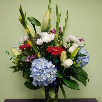 Mixed bouquet in a glass vase with blue hydrangeas, lilies, and gerbera daisies