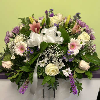 Mixed bouquet with pink lilies, roses, and purple flowers tied with a white ribbon