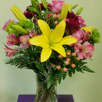 Bouquet of yellow lilies, pink roses, and mixed blooms in a glass vase