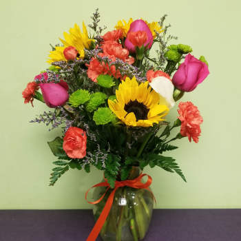 Mixed bouquet with sunflowers, pink roses, carnations, and a glass vase