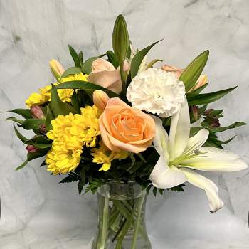 Peach roses, white lilies, and yellow daisies in a glass vase