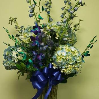 Blue hydrangea and orchid arrangement in a tall glass vase with a blue ribbon