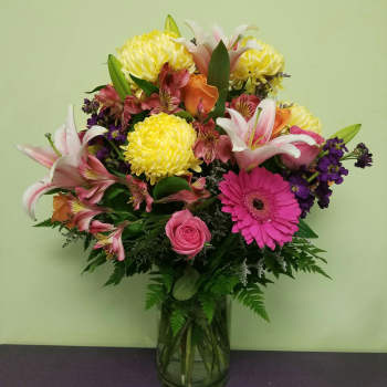 Mixed bouquet of lilies, roses, gerbera daisies, and chrysanthemums in a glass vase