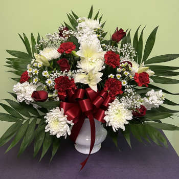 Red and white floral arrangement in a white vase with a red ribbon