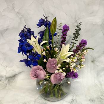 Mixed bouquet in a clear glass vase with blue, white, pink, and purple flowers
