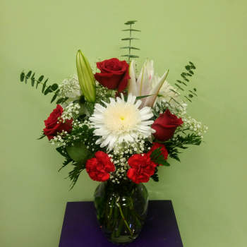 Bouquet of red roses, white lilies, and a white daisy in a glass vase