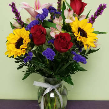 Bouquet of red roses, sunflowers, and pink lilies in a glass vase