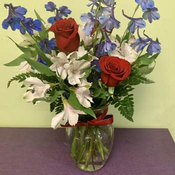 Bouquet of red roses, white alstroemeria, and blue delphinium in a glass vase