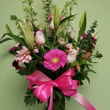Tall bouquet of pink lilies, gerbera daisies, and a bright ribbon in a glass vase