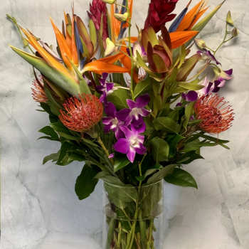 Tropical bouquet with orange bird-of-paradise and purple orchids in a glass vase