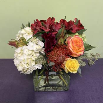 Mixed bouquet in a square glass vase with red, white, orange, and yellow flowers