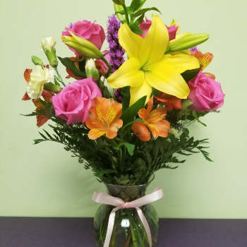 Bouquet of pink roses, yellow lilies, and orange alstroemeria in a glass vase