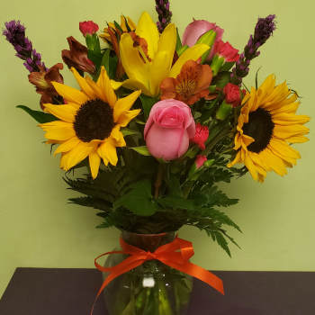 Bouquet of sunflowers, roses, and mixed blooms in a glass vase with an orange ribbon