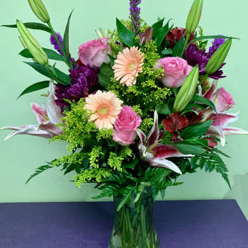 Mixed bouquet of pink roses, lilies, and purple flowers in a glass vase