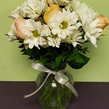 White daisies and pale peach roses in a glass vase with a ribbon