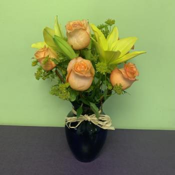 Peach roses and yellow lilies in a black vase with a raffia bow