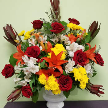 Mixed bouquet of red roses, orange lilies, and yellow chrysanthemums in a white vase
