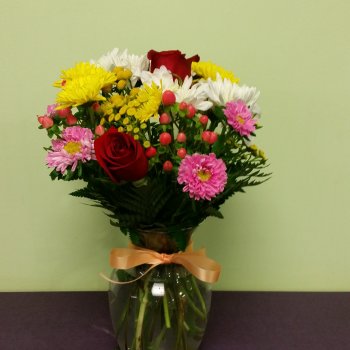Mixed bouquet of roses and daisies in a glass vase with a ribbon