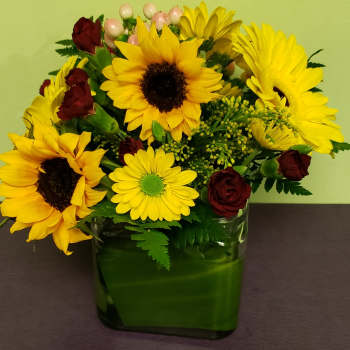 Sunflower and burgundy rose arrangement in a green glass vase