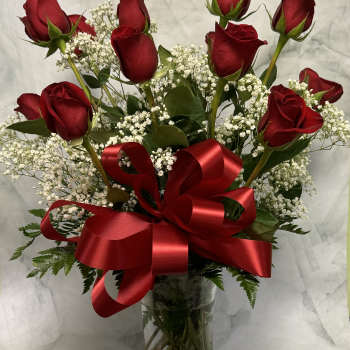 Red roses in a clear glass vase with baby's breath and a red ribbon bow