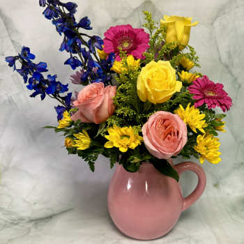 Mixed bouquet of pink, yellow, and blue flowers in a pink pitcher vase