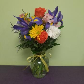 Mixed bouquet of roses, irises, daisies, and carnations in a glass vase