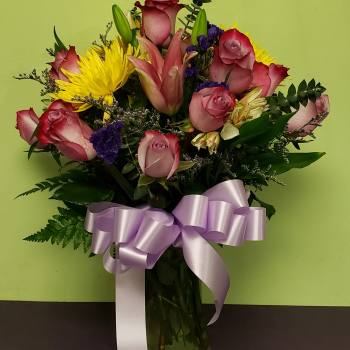 Bouquet of pink roses and yellow lilies in a glass vase with a lavender ribbon