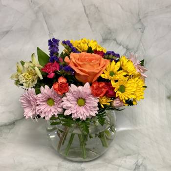 Mixed bouquet in a clear glass vase with an orange rose, daisies, and colorful filler flowers