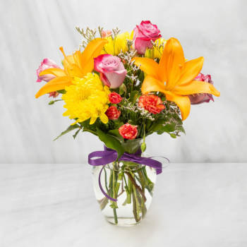 Bouquet of orange lilies, pink roses, and yellow mums in a glass vase