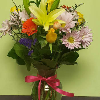 Mixed bouquet with a yellow lily in a glass vase tied with a pink ribbon