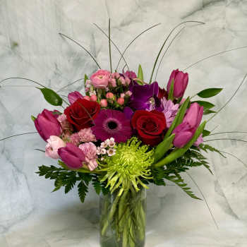 Mixed bouquet of pink, red, and purple flowers in a glass vase