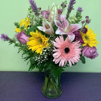 Mixed bouquet of pink lilies, roses, gerbera daisies, and sunflowers in a glass vase