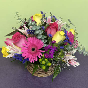 Basket arrangement with pink roses, gerbera daisies, lilies, and purple filler flowers