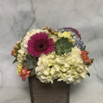 Mixed flowers in a dark wooden box with a bright pink daisy-like bloom