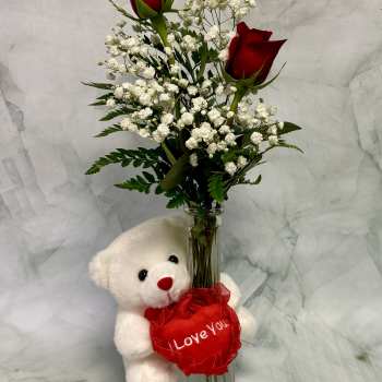 Two red roses in a glass vase with a teddy bear holding a heart