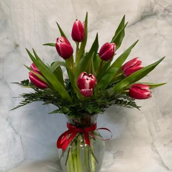 Pink tulips arranged in a clear glass vase with a red ribbon
