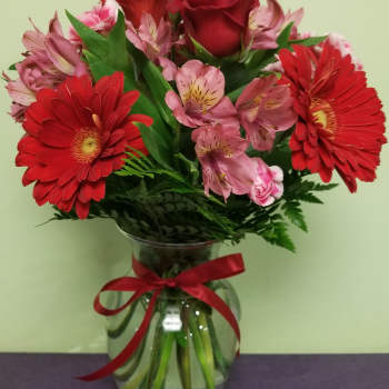 Red gerbera daisies and pink roses in a glass vase with a red ribbon