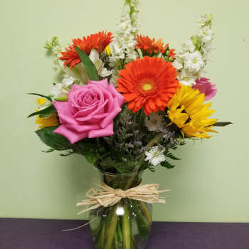 Mixed bouquet of pink, orange, and yellow flowers in a glass vase