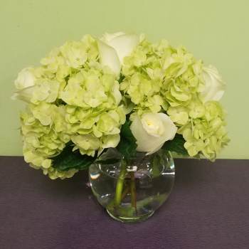 White roses and pale green hydrangeas in a clear glass vase