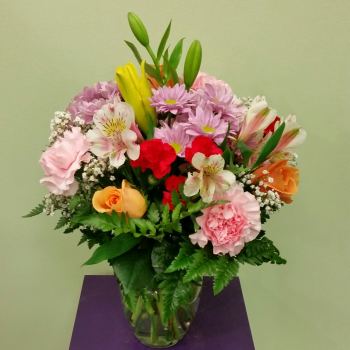 Mixed bouquet of pink, red, yellow, and orange flowers in a glass vase