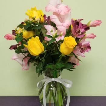 Bouquet of yellow roses and pink alstroemeria in a glass vase with a white ribbon