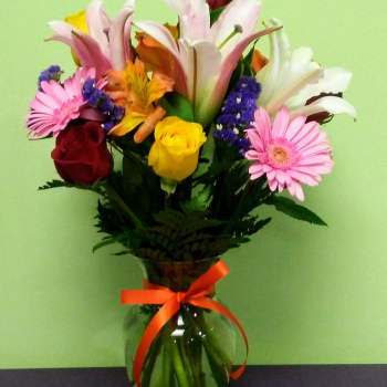 Mixed bouquet of lilies, roses, and daisies in a glass vase with a ribbon