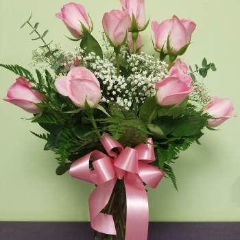 Pink roses in a glass vase with baby's breath and a pink ribbon