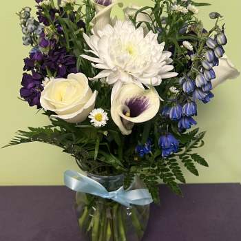 Bouquet of white, purple, and blue flowers in a glass vase with a blue ribbon