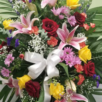 Standing floral spray with roses, lilies, and a white ribbon bow