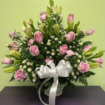 Pink roses and lilies arranged in a vase with a white ribbon bow